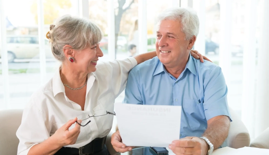 Pareja de personas mayores sonriendo con documento en mano.