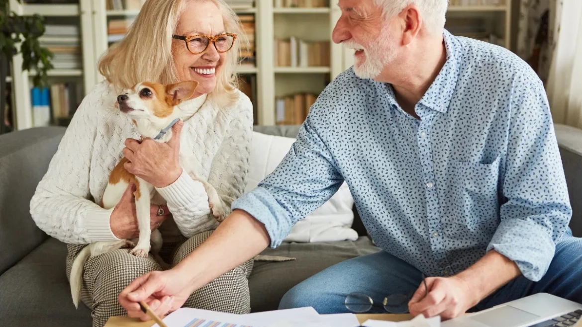 Pareja de personas mayores sonriendo con perrito y con documento para firmar.